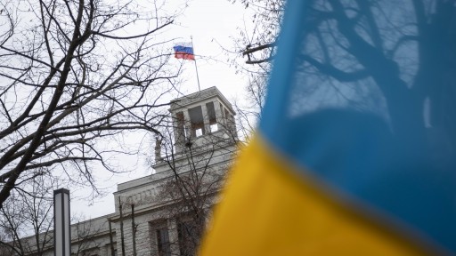 Eine ukrainische Fahne im Vordergrund, dahinter ist eine russische Flagge auf einem Gebäude zu sehen. (Foto: IMAGO / A. Friedrichs)